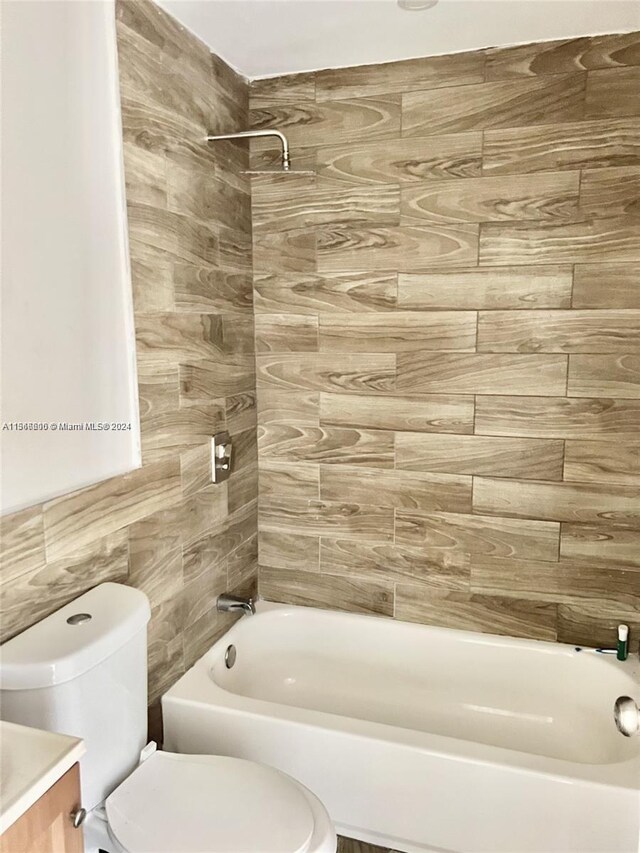 full bathroom featuring tiled shower / bath, vanity, toilet, and tile walls