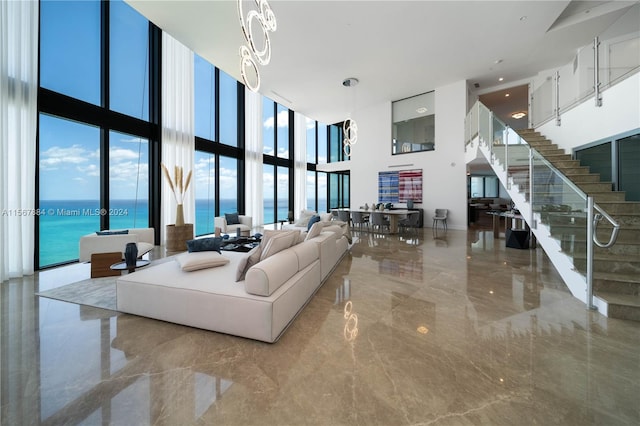 tiled living room featuring floor to ceiling windows, a water view, a towering ceiling, and a notable chandelier