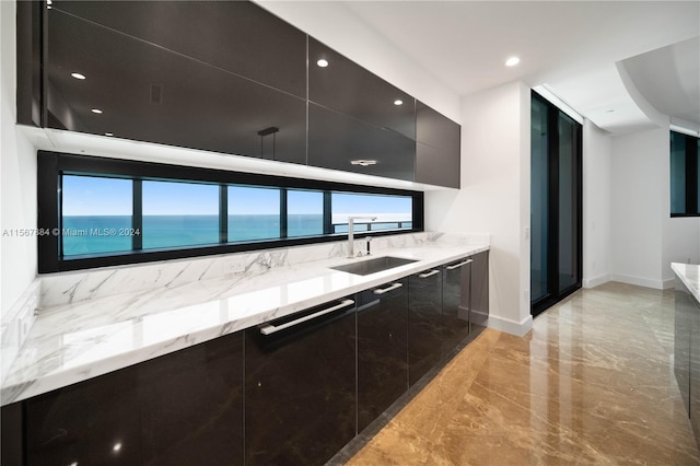 kitchen featuring light stone counters, light tile floors, sink, and a water view