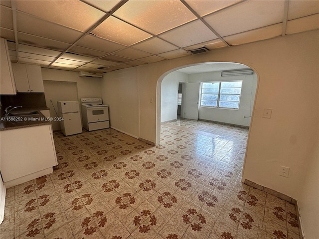 kitchen with light tile floors, a drop ceiling, white appliances, sink, and white cabinetry