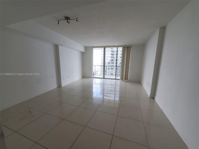 tiled empty room featuring a wall of windows and a textured ceiling