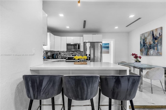 kitchen with light tile flooring, kitchen peninsula, stainless steel appliances, tasteful backsplash, and white cabinetry