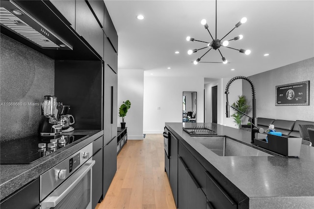 kitchen with black electric cooktop, stainless steel oven, a chandelier, light wood-type flooring, and sink