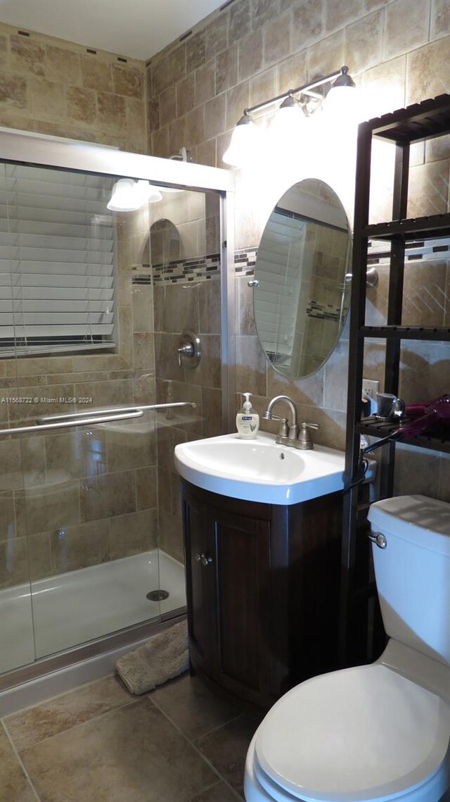 bathroom with tile walls, toilet, tile flooring, an enclosed shower, and vanity