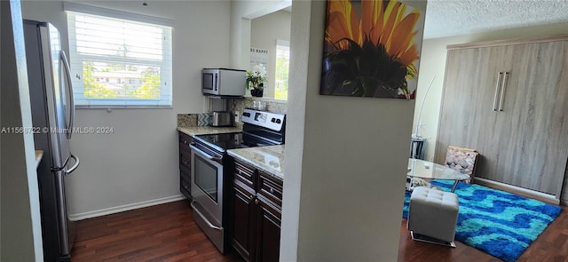 kitchen featuring appliances with stainless steel finishes, dark wood-type flooring, a textured ceiling, and light stone countertops