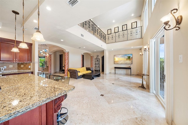 interior space featuring decorative light fixtures, light stone counters, backsplash, and a high ceiling