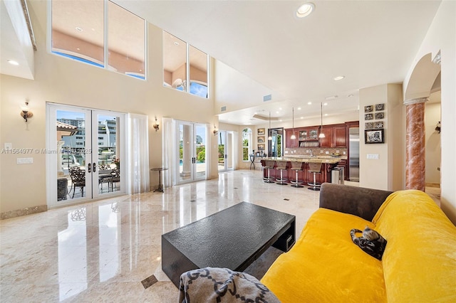 living room featuring decorative columns, a towering ceiling, and french doors