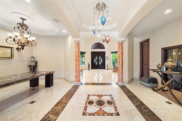 foyer entrance with a tray ceiling, ornate columns, and a chandelier