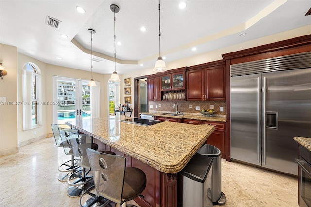 kitchen with a raised ceiling, a center island, built in refrigerator, and hanging light fixtures