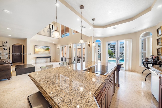 kitchen featuring light stone countertops, french doors, black electric stovetop, pendant lighting, and a kitchen island