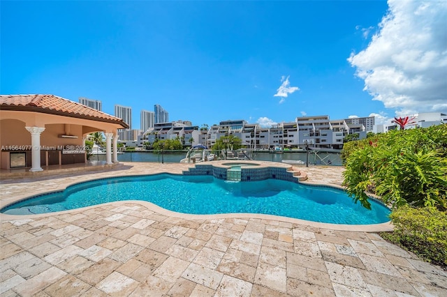 view of swimming pool with a patio area, a water view, and an in ground hot tub