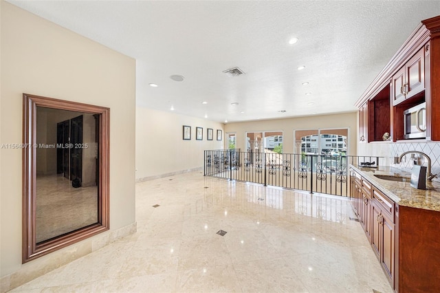 kitchen with sink, decorative backsplash, light stone countertops, and a textured ceiling