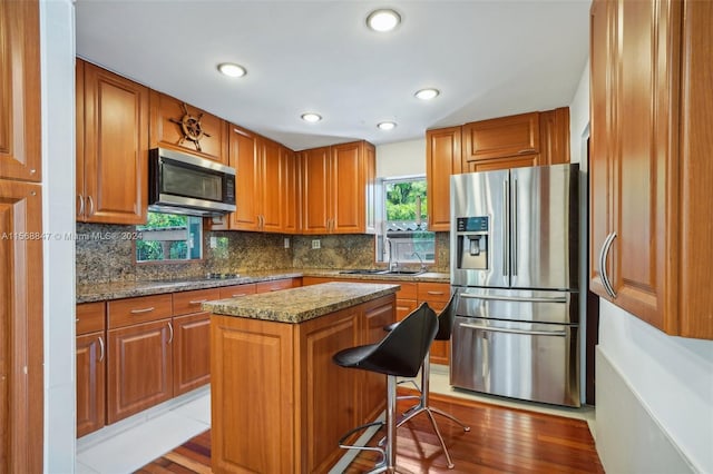 kitchen featuring a breakfast bar area, appliances with stainless steel finishes, light stone countertops, a kitchen island, and sink