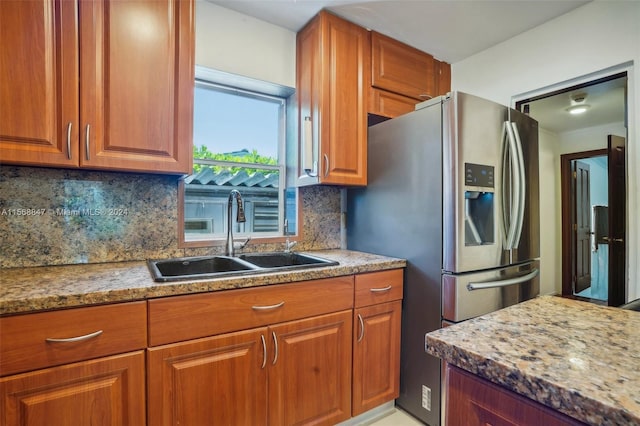 kitchen with backsplash, light stone countertops, sink, and stainless steel refrigerator with ice dispenser