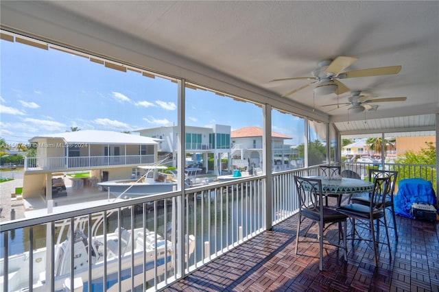 sunroom with ceiling fan and a water view