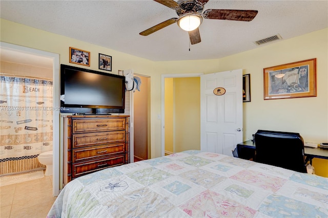 tiled bedroom with a textured ceiling, ensuite bath, and ceiling fan