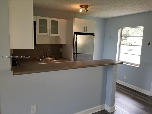 kitchen featuring kitchen peninsula, stainless steel fridge, hardwood / wood-style flooring, white cabinetry, and sink