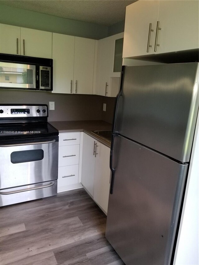 kitchen with appliances with stainless steel finishes, hardwood / wood-style floors, and white cabinetry