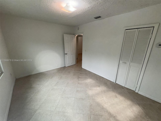 unfurnished bedroom with a closet, a textured ceiling, and light tile floors