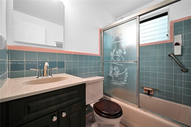 full bathroom featuring bath / shower combo with glass door, vanity, tile walls, and toilet