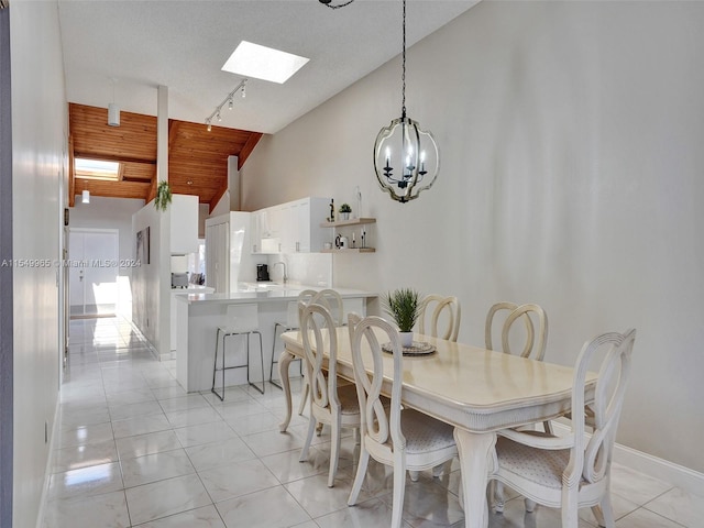 tiled dining area with high vaulted ceiling, rail lighting, a textured ceiling, a skylight, and an inviting chandelier