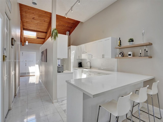 kitchen with lofted ceiling with skylight, light tile floors, white cabinetry, wooden ceiling, and a kitchen breakfast bar