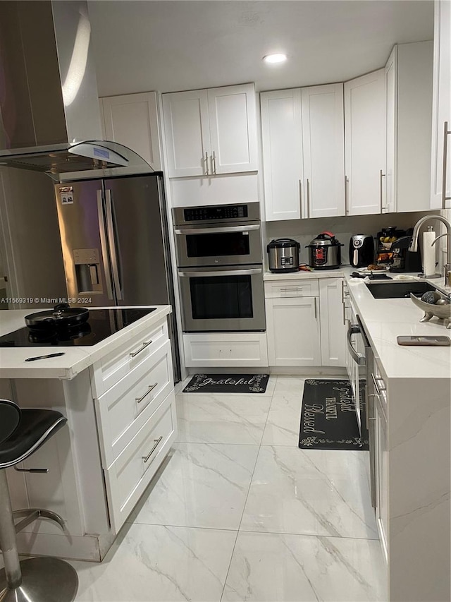 kitchen featuring light tile floors, white cabinetry, a breakfast bar area, stainless steel appliances, and extractor fan