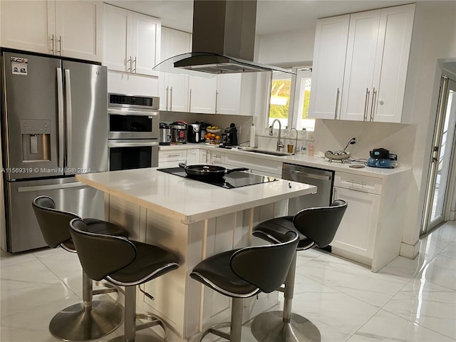 kitchen with appliances with stainless steel finishes, a breakfast bar area, wall chimney exhaust hood, white cabinetry, and a center island