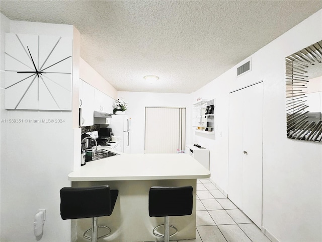 kitchen with white cabinets, kitchen peninsula, a textured ceiling, a kitchen bar, and light tile patterned floors