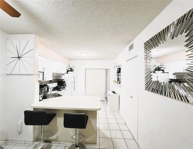 kitchen featuring white cabinetry, range with electric stovetop, white fridge, a textured ceiling, and a kitchen bar