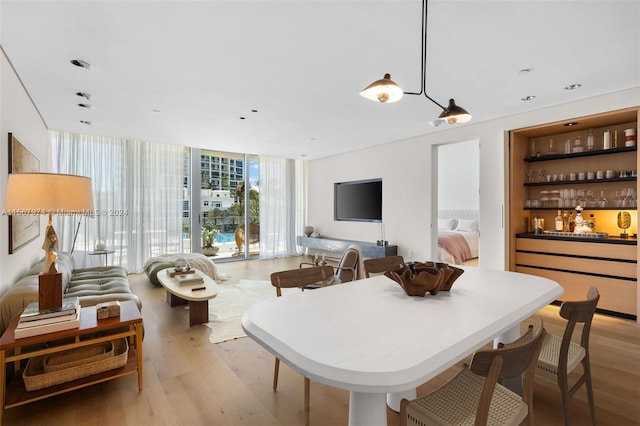 dining space with bar area, expansive windows, and light wood-type flooring