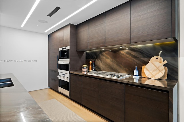 kitchen with stainless steel gas stovetop, double oven, dark brown cabinets, and tasteful backsplash