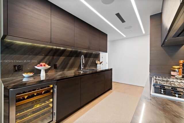 bar featuring dark brown cabinets, wine cooler, stainless steel gas stovetop, sink, and decorative backsplash