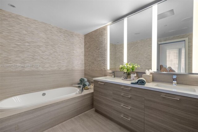 bathroom with tiled tub, vanity, and tile walls