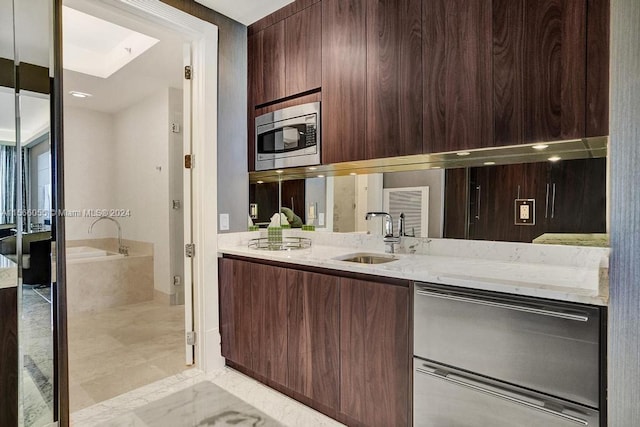 kitchen with sink, stainless steel microwave, light tile floors, and light stone counters