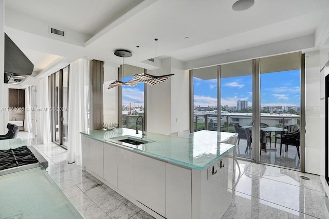 kitchen featuring white cabinetry, sink, decorative light fixtures, light stone counters, and a wealth of natural light