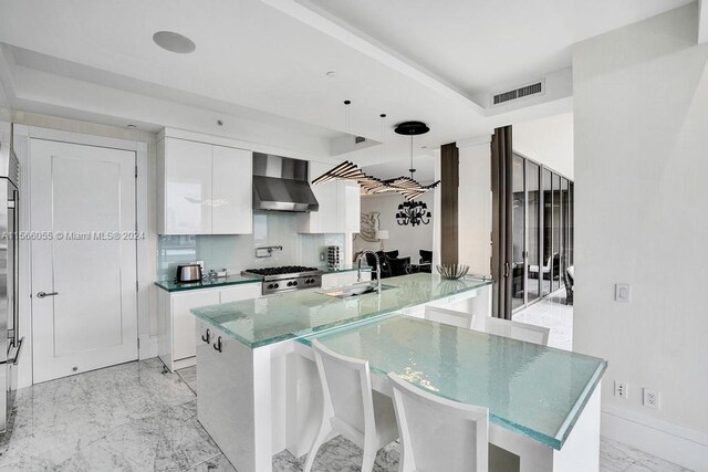 kitchen with hanging light fixtures, white cabinets, wall chimney range hood, a breakfast bar area, and tasteful backsplash