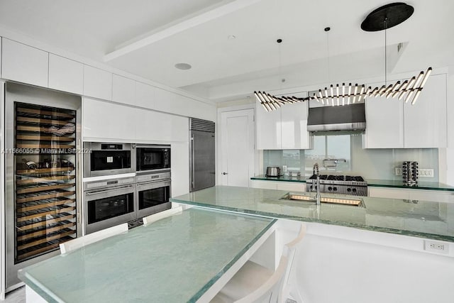 kitchen with wall chimney exhaust hood, hanging light fixtures, and white cabinets