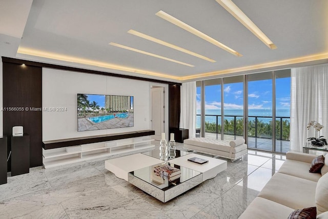 living room with floor to ceiling windows, a raised ceiling, light tile floors, and a water view