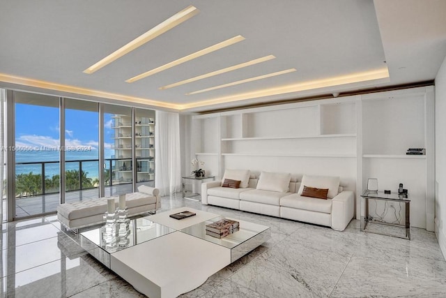 living room with floor to ceiling windows, a raised ceiling, light tile floors, and a water view