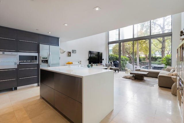 kitchen featuring expansive windows, a kitchen island, white oven, light tile flooring, and stainless steel refrigerator with ice dispenser