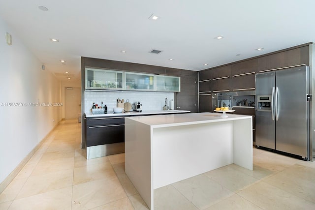 kitchen with dark brown cabinets, backsplash, stainless steel appliances, light tile flooring, and a center island