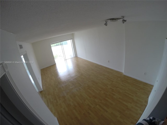 spare room with a textured ceiling, light hardwood / wood-style floors, and track lighting