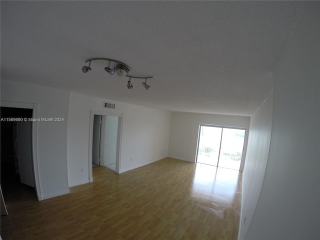 unfurnished room with a textured ceiling, light hardwood / wood-style floors, and track lighting