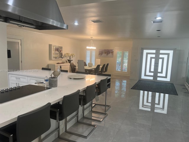 kitchen featuring wall chimney exhaust hood, dark tile floors, white cabinets, a breakfast bar, and a notable chandelier