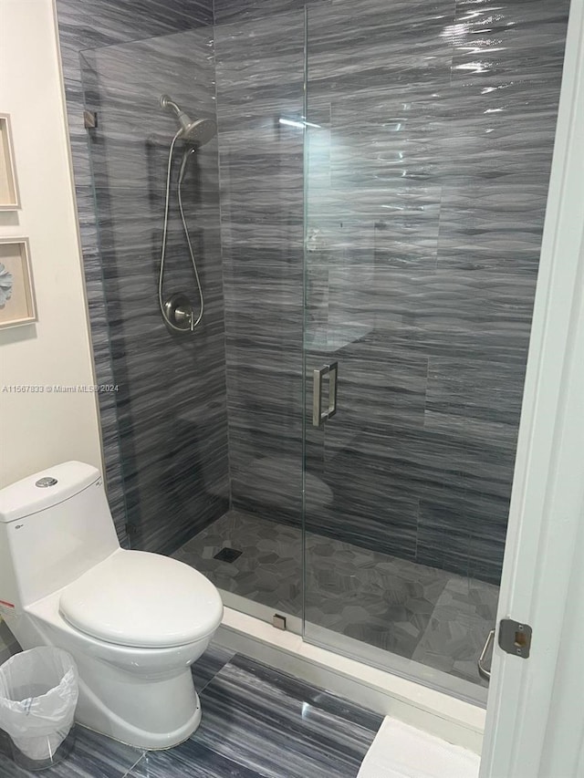 bathroom with a shower with shower door, toilet, and tile flooring