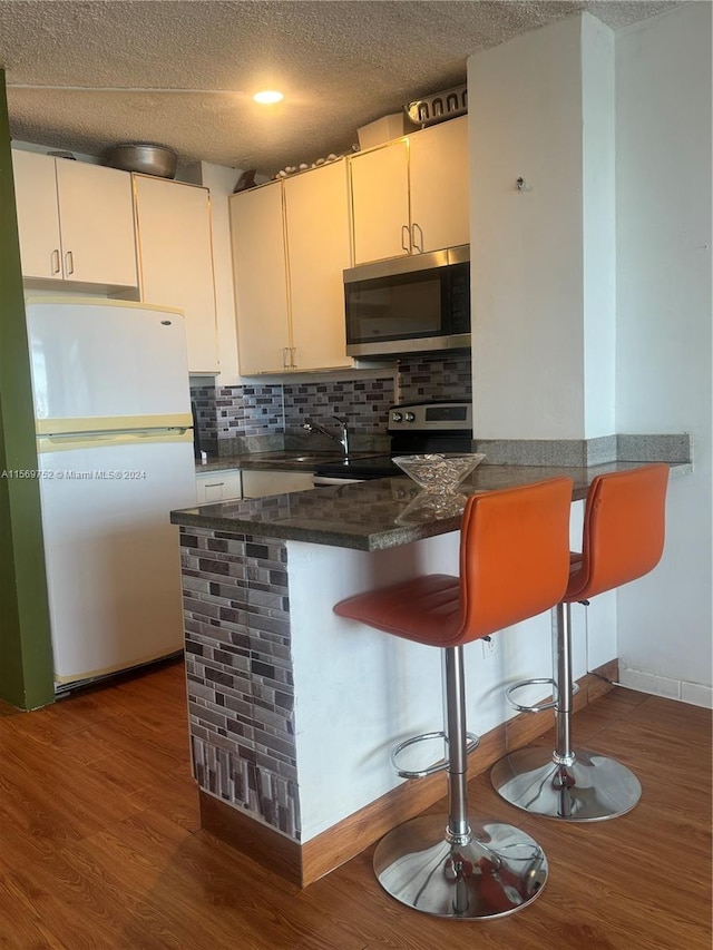 kitchen with kitchen peninsula, stainless steel appliances, tasteful backsplash, dark wood-type flooring, and white cabinets