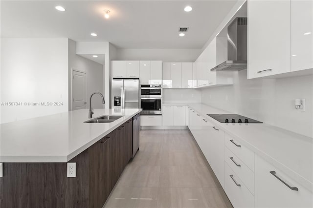 kitchen featuring sink, white cabinetry, stainless steel appliances, a center island with sink, and wall chimney exhaust hood