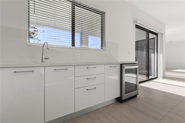 kitchen featuring sink, beverage cooler, light tile patterned floors, and white cabinets