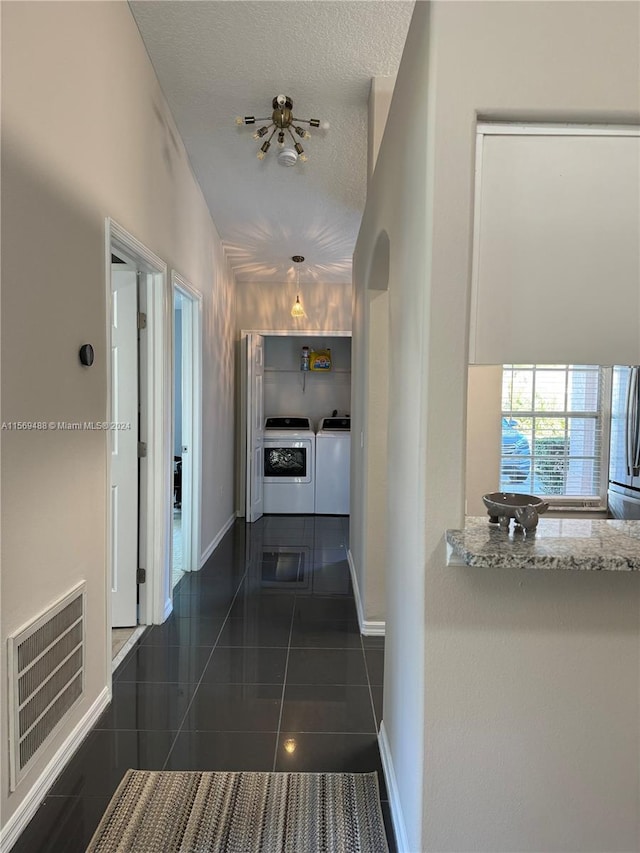 hallway with dark tile floors, washing machine and clothes dryer, and a textured ceiling